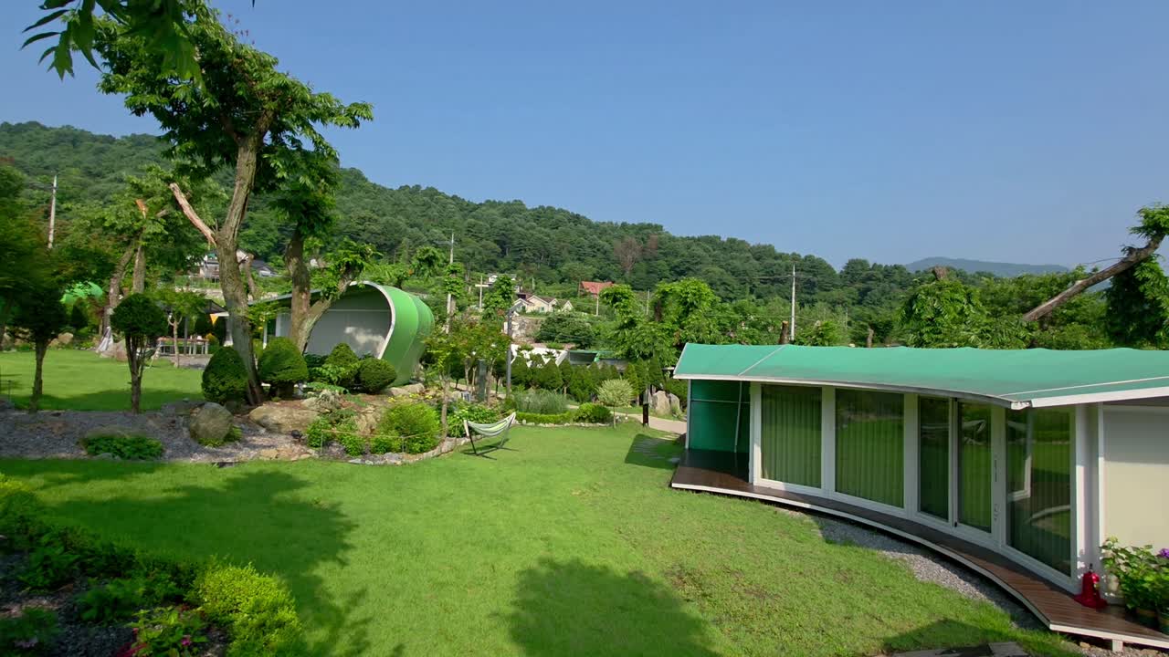 Leaf-inspired glamping cabins and a modern BBQ pavilion nestle in a lush garden surrounded by trees and greenery at Glamtree Resort in Gapyeong Mountains, South Korea