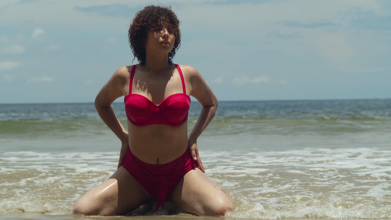 Basking in the sunlight, a girl with curly hair and a red bikini strolls along a tropical island beach