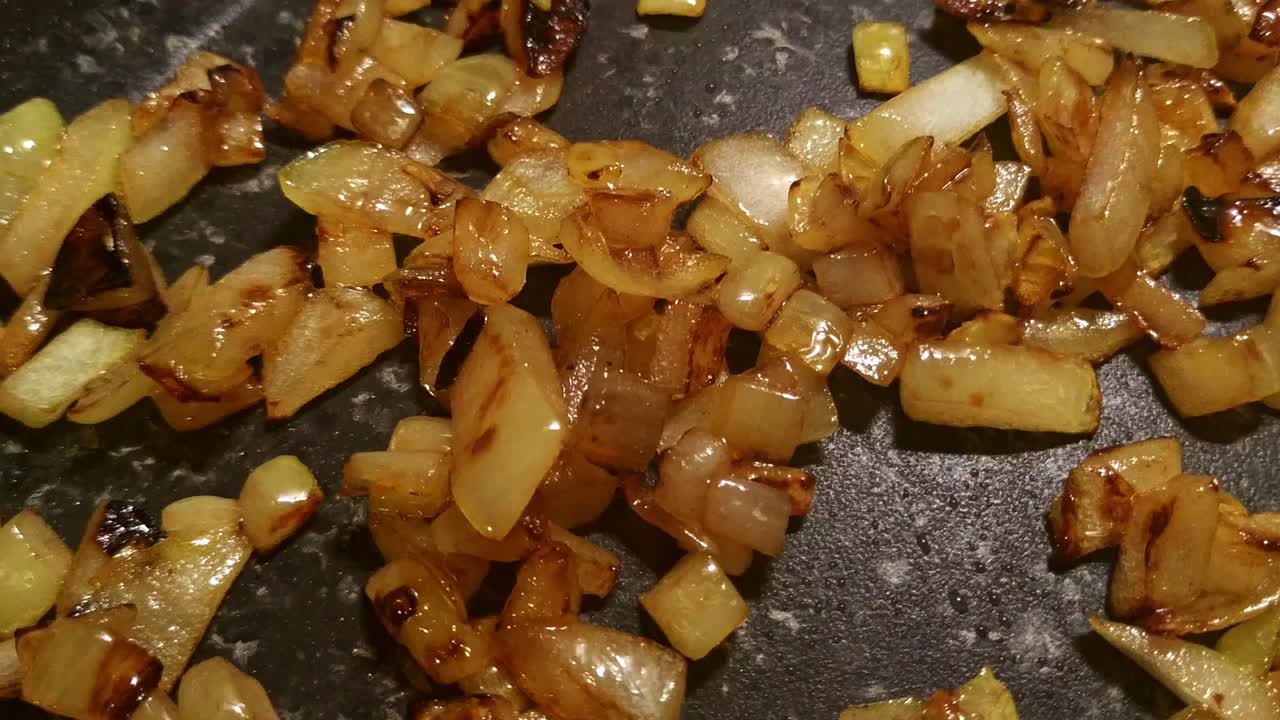 Close up of white onions cooking until they are golden brown with some bubbling as they sizzle in the frying pan