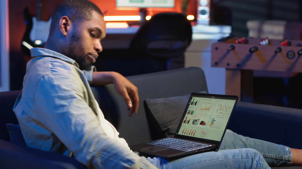Black male trader monitoring stock market real time changes on laptop