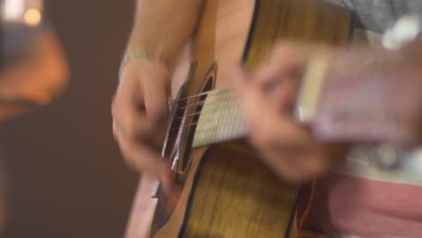 close up of a professional musician playing chords on a western guitar with a blurred drummer in the background during a live session with warm studio lights