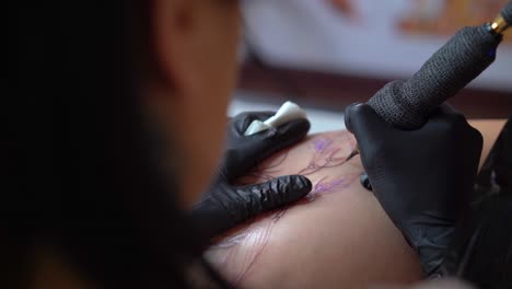 tattooist applying tattoo on hip of anonymous woman in shop