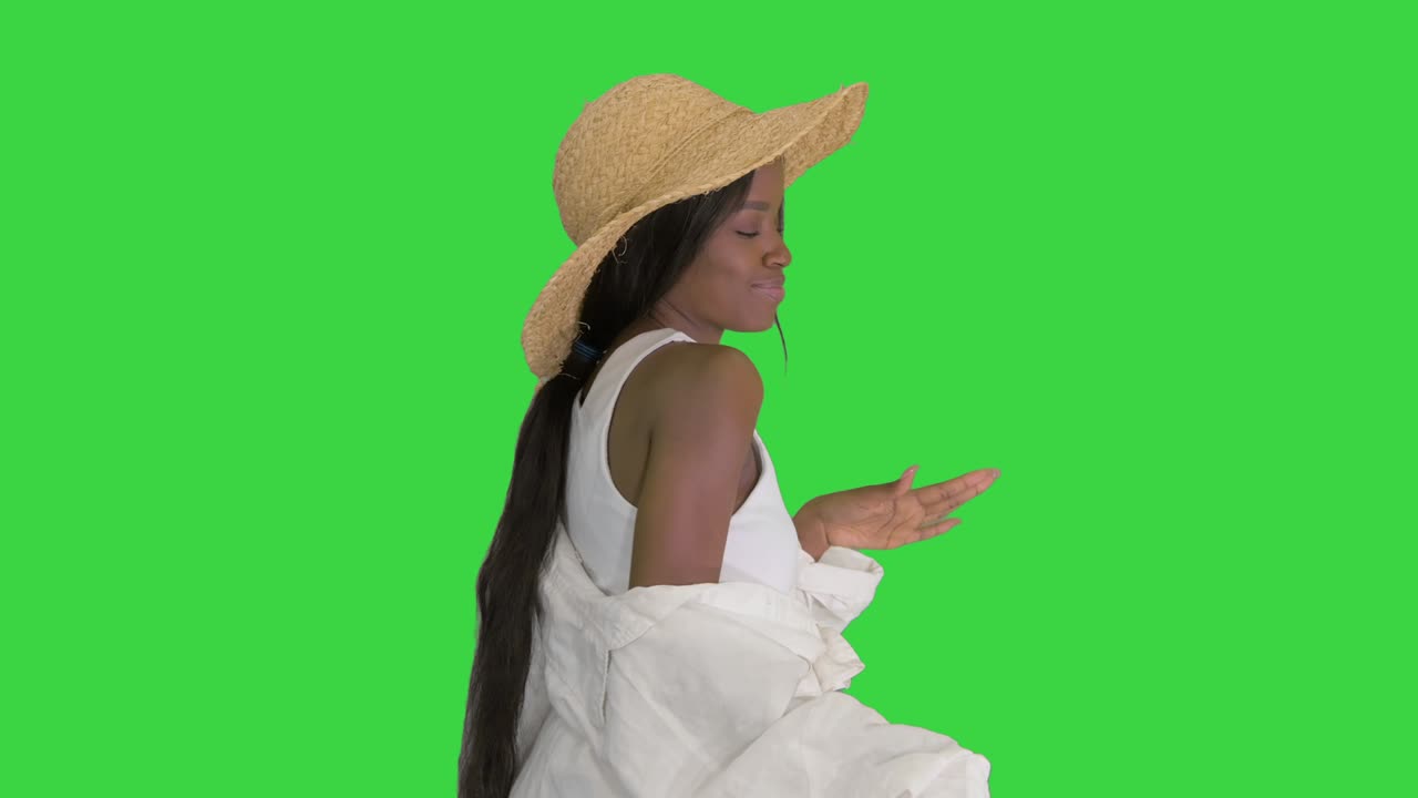 una alegre chica afroamericana con un sombrero de paja bailando en una pantalla verde, clave de croma