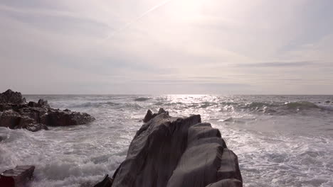 left to right pan of waves breaking against a rocky cove on a summer’s evening in slow motion