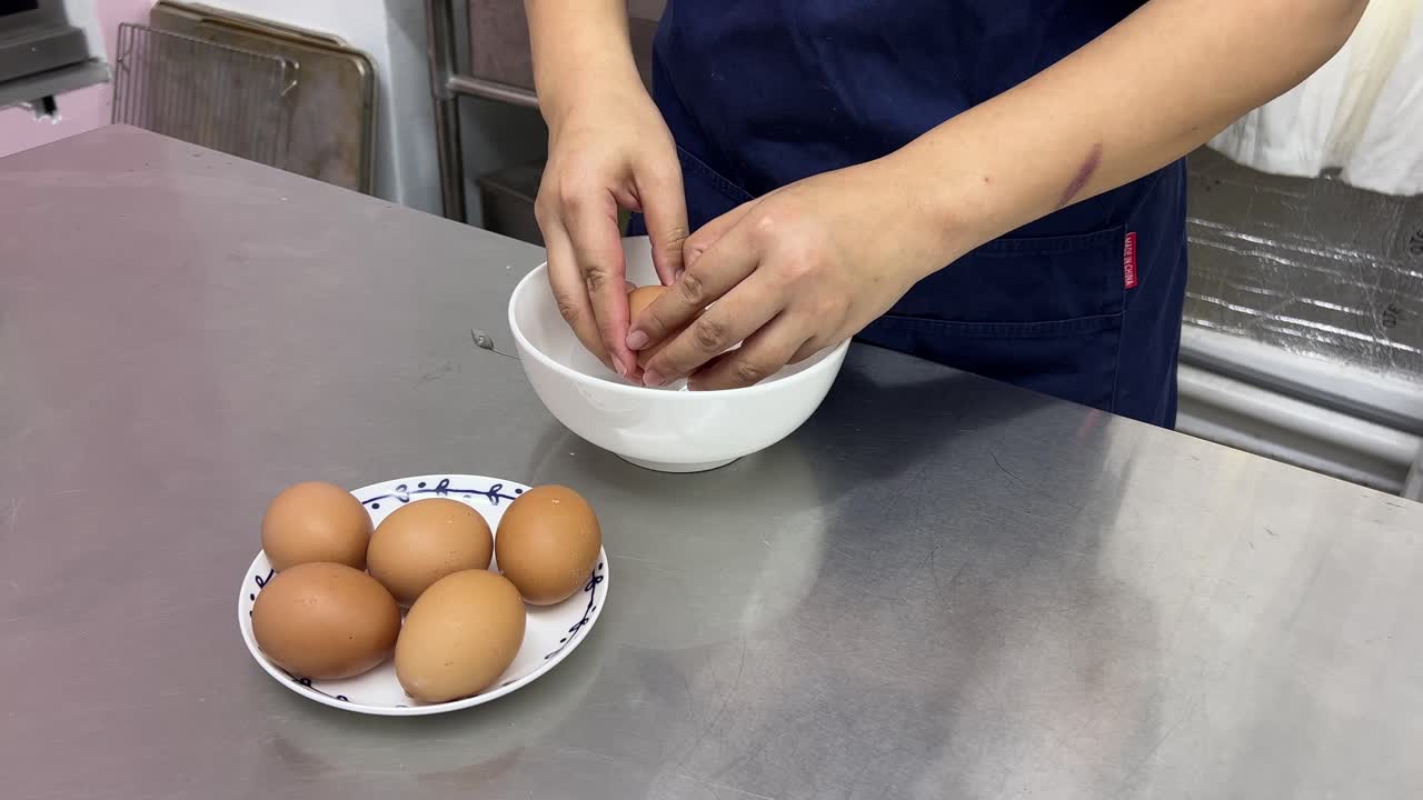 elaboración de postres de pastelería en curso, pastelero rompiendo huevos en un ambiente de restaurante comercial de tazón