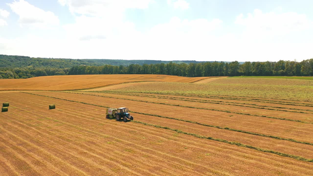 Aerial view on the field and tractor working on the natural rural background. Flight over agricultural field during grass harvest for livestock.