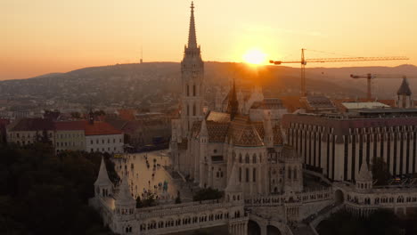 Sun-disappears-behind-the-silhouette-of-the-Matthias-Church,-casting-a-tranquil-orange-glow-over-the-landscape