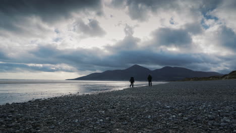 Paar-Zu-Fuß-Am-Strand-In-Richtung-Der-Berge-Bei-Kühlem-Frühlingswetter