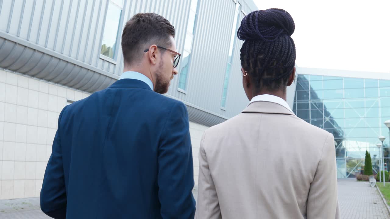 Rear view of caucasian businessman and african american businesswoman walking down the street and talking about work