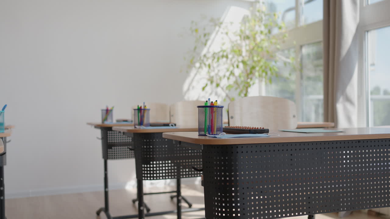 Rays of light falling to the empty dark classroom. The camera panning behind rows of desks and chairs. Teaching class without students during a break. Abandoned school. Disturbing mood.