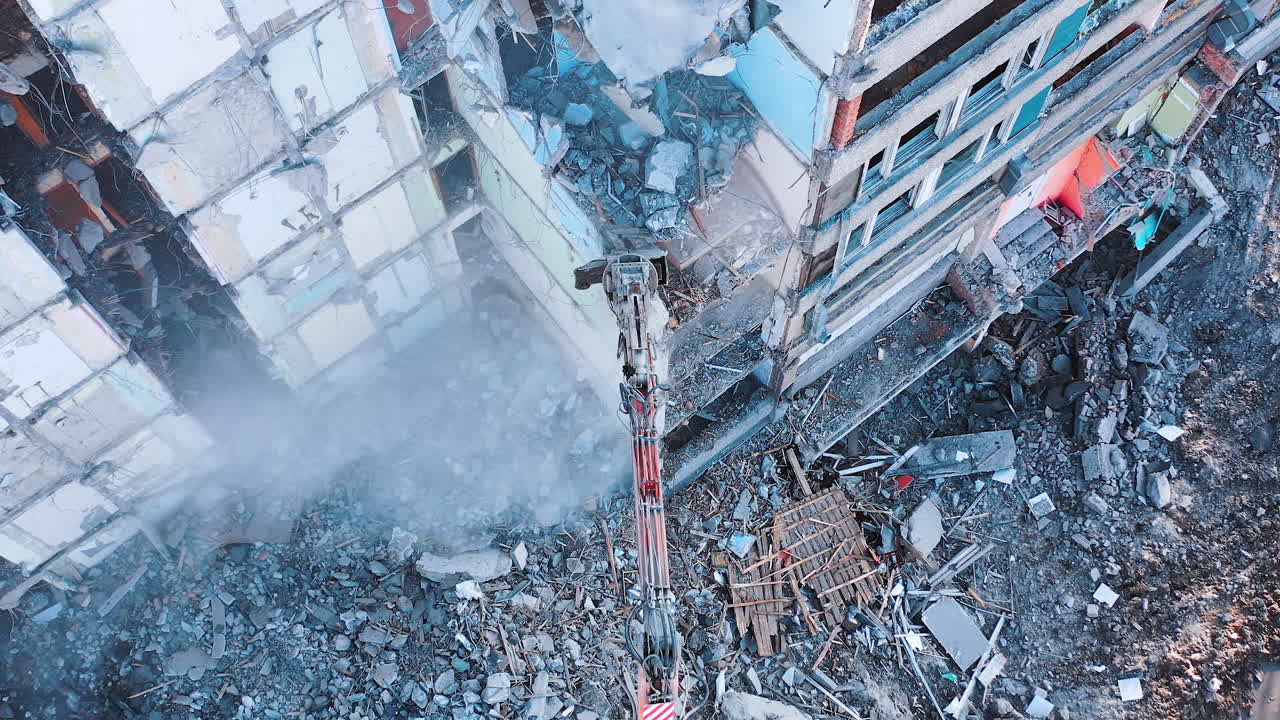 Demolishing machinery breaks the floors and walls of the ruin. Debris falling down with heavy dusty clouds. Rising over the ruins and debris.