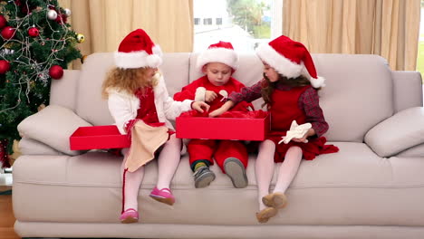 cute festive siblings opening christmas gifts on the couch