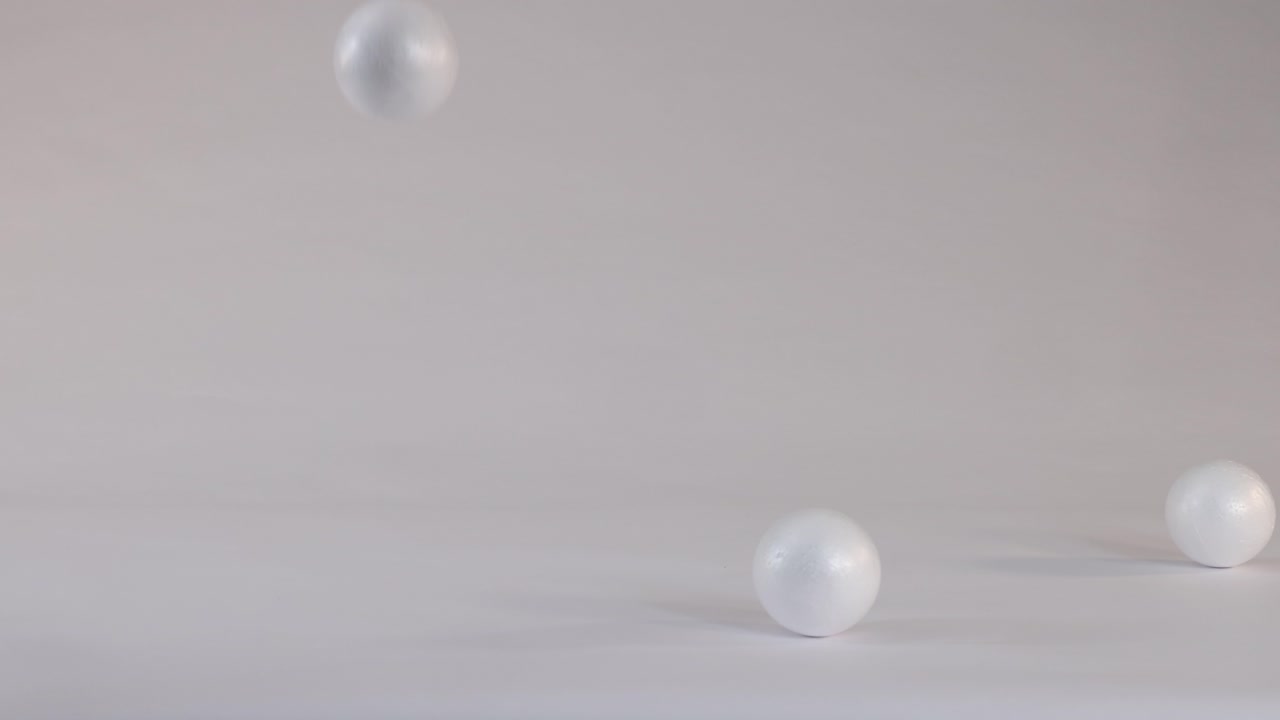 Lightweight white foam spheres bounce and roll across a neutral grey studio floor surface