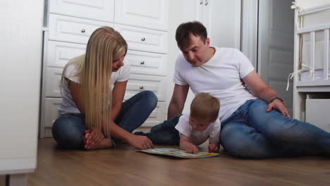 A-family-of-three-in-white-T-shirts-and-blue-jeans-sitting-on-the-floor-of-their-bedroom-playing-with-the-boy-in-intellectual-games.-Slow-motion-shooting-happy-family