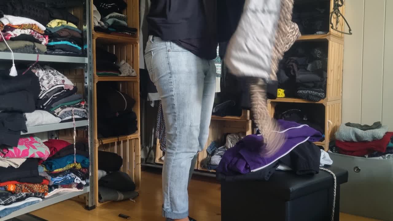 A woman in jeans folds used clothes, trying to bring order to her untidy, chaotic open wardrobe at home in Bern, Switzerland