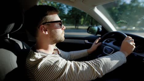 un hombre está conduciendo un coche moderno. un hombre guapo con una barba en las gafas protectoras del sol, con confianza dirige