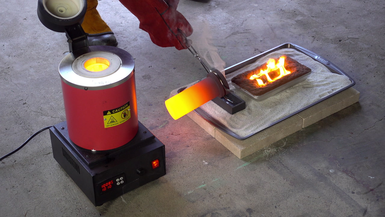 Yellow-hot crucible is removed from furnace and molten brass poured into molds. Crucible replaced in furnace.