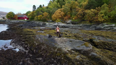 Aerial-footage-closing-in-on-a-man-standing-at-the-shore-and-taking-pictures-with-a-camera