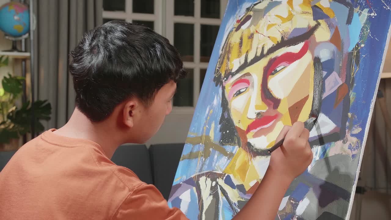Close Up Side View Of An Asian Artist Boy Holding Paintbrush Mixed Colour And Painting A Girl'S Face On The Canvas