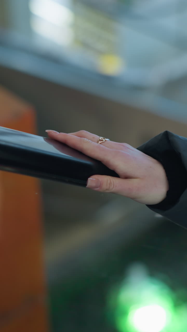 Close-up of hand with a ring placed on rail of moving escalator with colorful blinking lights reflecting in blurred background, escalator ascending in shopping mall environment