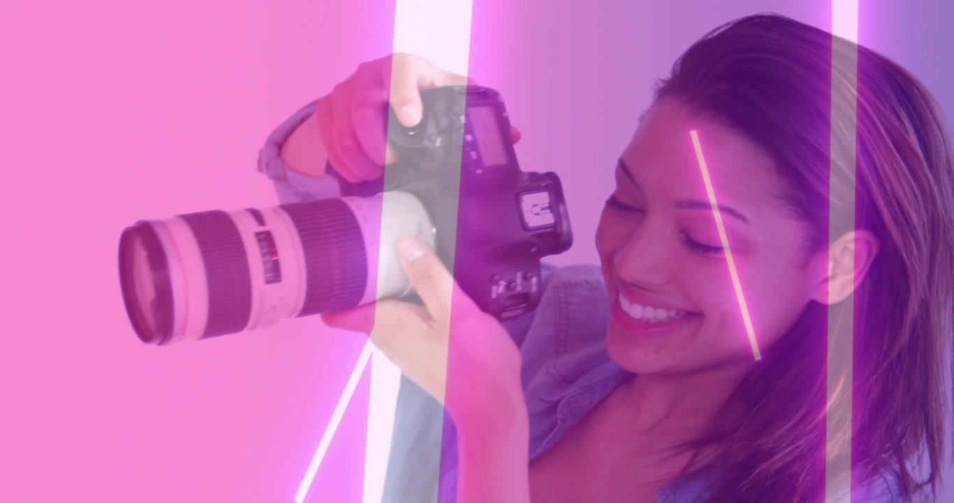Mulher fotógrafa levantando câmera em estúdio, causando rastros rosa neon, capturando e revisando a foto