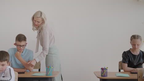 female teacher controlling learning process in primary school. a female teacher walks between the desks and looks after the completion of the task