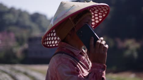 woman in conical hat talking on phone in rural agricultural setting