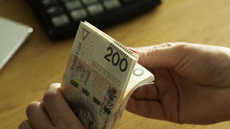 Female-hands-holding-200-Polish-zloty-bills-over-the-table---wealth-concept,-close-up-shot