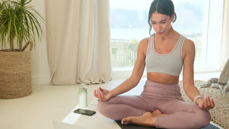 practicing yoga, woman meditating at home with smartphone and water bottle nearby