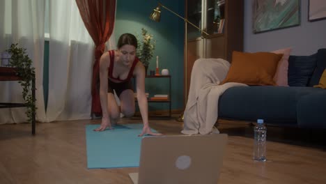 joven en forma haciendo ejercicios de estiramiento de yoga con computadora portátil en línea en casa. auto-aislación durante el bloqueo de coronavirus, educación remota deportiva en internet. concepto de estilo de vida saludable, gimnasio en casa