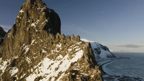 Aerial-view-of-a-flock-of-birds-flying-around-rocky-peaks,-winter-sunset-in-Iceland