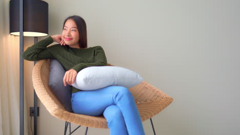 young asian woman reclining on a rattan lounger while looking out of hotel room window