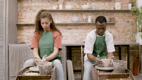 Front View Of Employees Wearing Green Apron Modeling Ceramic Pieces On Potter Wheel In A Workshop