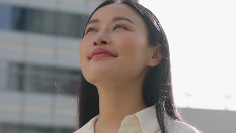 portrait of a confident young asian woman looking upwards in a city