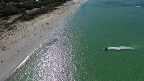 Vista-Aérea,-Scooter-De-Agua-Acercándose-A-La-Playa-De-Arena-Blanca-En-La-Pintoresca-Costa-Australiana-En-Un-Día-Soleado,-Disparo-De-Drones-En-órbita