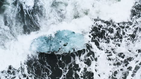 Atemberaubende-Drohnenaufnahme-Von-Wellen,-Die-Auf-Einem-Wunderschönen-Eisfelsen-Am-Diamond-Beach-In-Island-Brechen