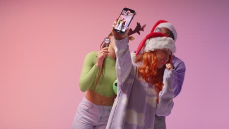 studio shot of gen z friends dancing and posing for selfie at christmas party wearing santa hat and reindeer antlers 1