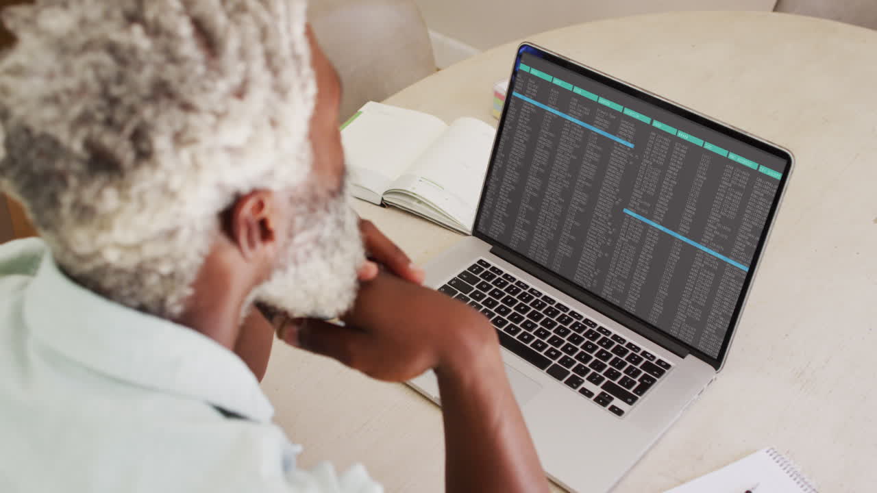 African american man sitting at desk watching coding data processing on laptop screen