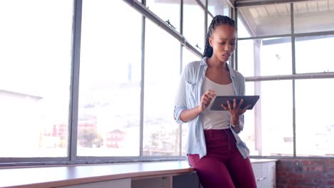 mujer de negocios afroamericana casual usando tableta por la ventana en la oficina, cámara lenta, espacio de copia