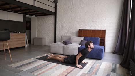 Un-Joven-Sano-Practica-Yoga-En-Una-Alfombra,-Parado-En-Pose-De-Cobra