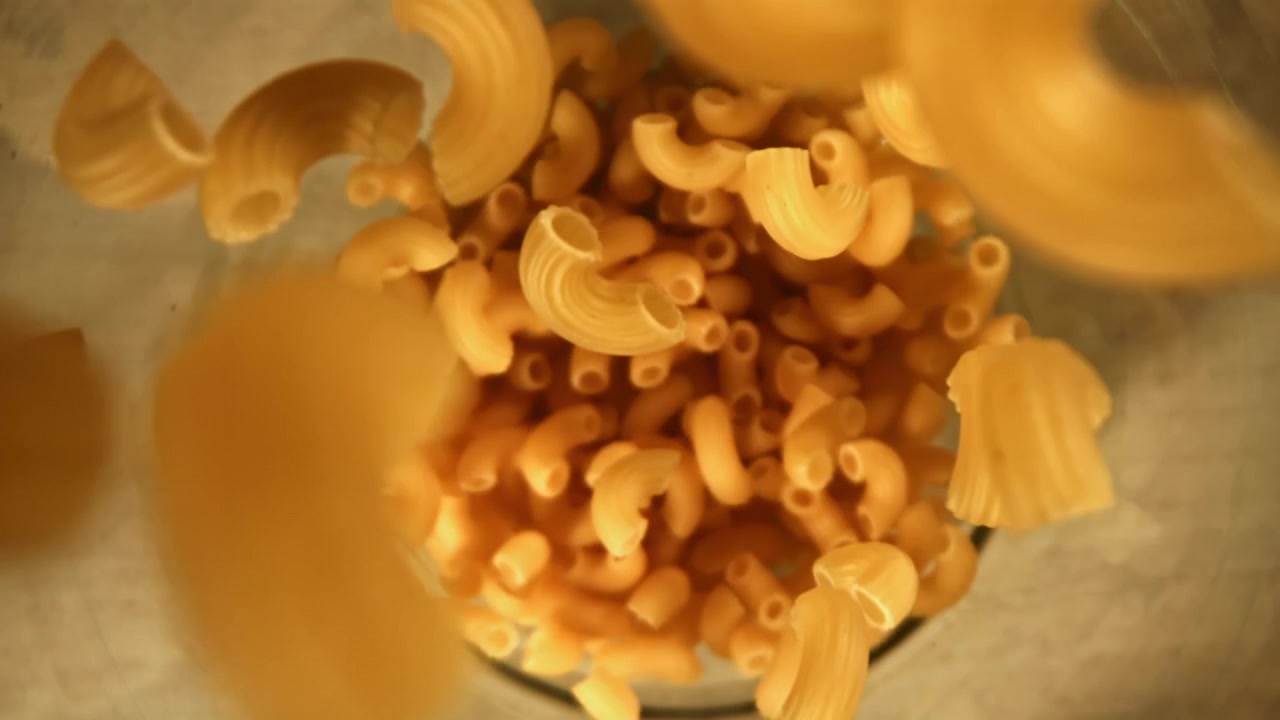 Maccheroni secchi che cadono in una ciotola di vetro al rallentatore