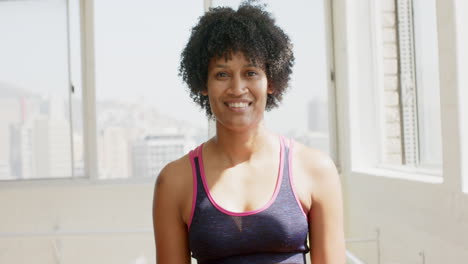 mujer biracial con cabello rizado sonriendo, con ropa deportiva