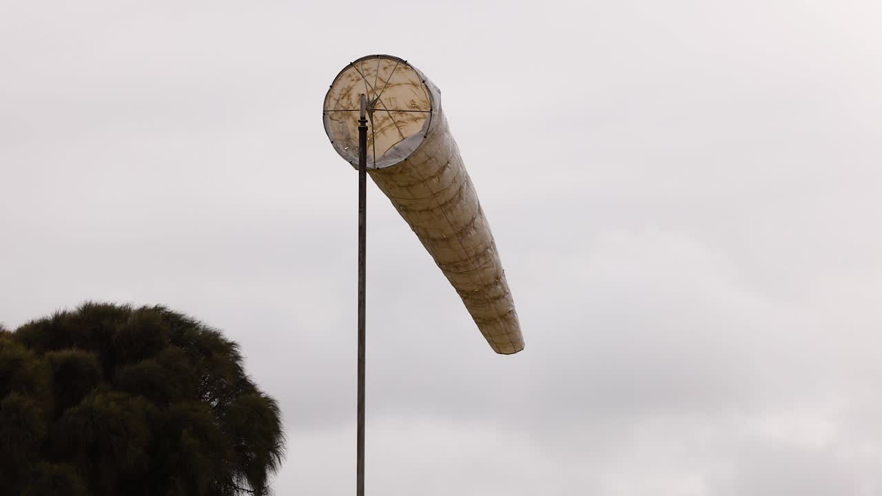 A windsock sways in the breeze at Port Campbell, Australia, under overcast skies, capturing the dynamic coastal wind patterns