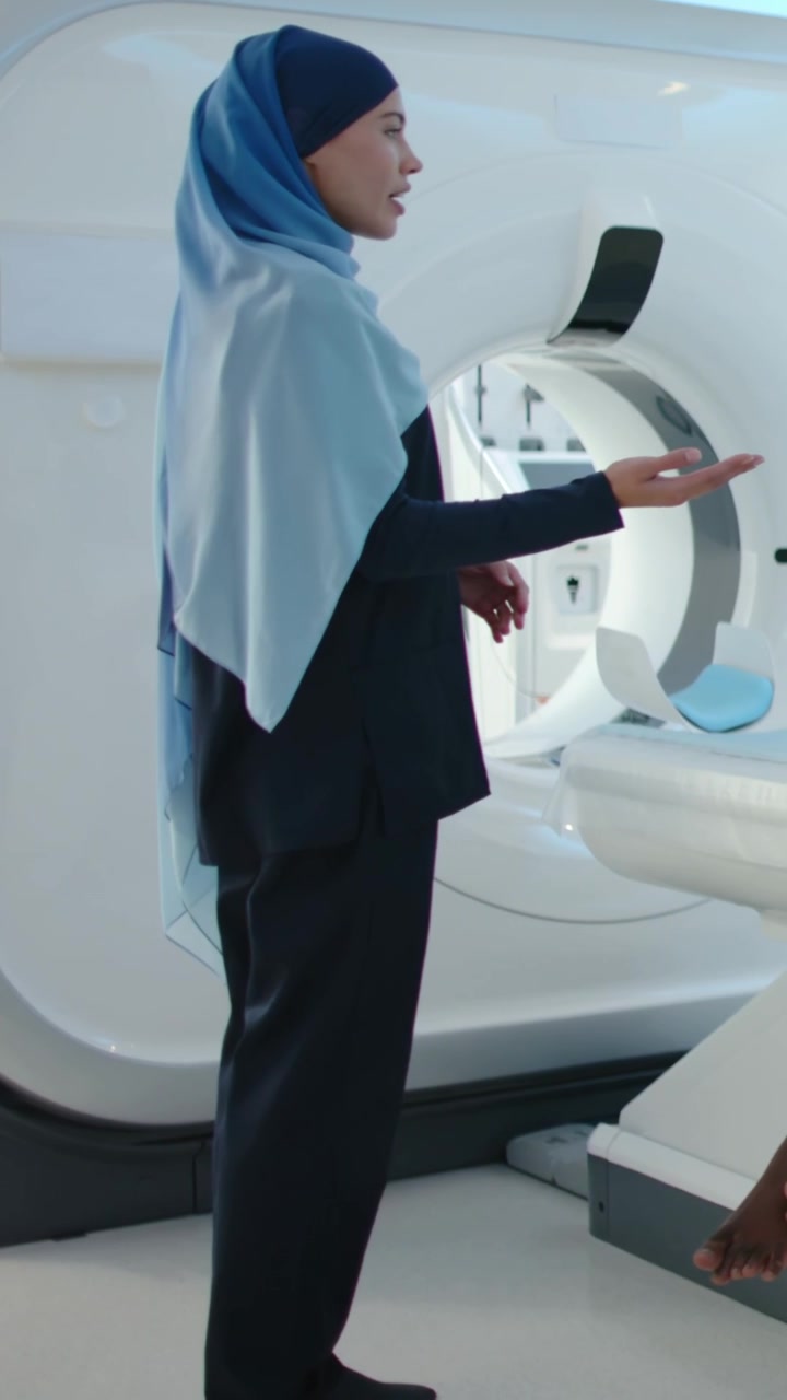 Video verticale: Tecnica con hijab blu che istruisce il paziente prima della TAC sul lettino dello scanner TC