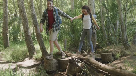 Happy-african-american-couple-wearing-backpacks-and-hiking-in-forest,-slow-motion