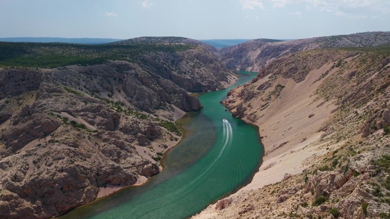 Høyt luftfoto av en båt som suser gjennom den smaragdgrønne Zrmanja-elvecanyonen i Kroatia
