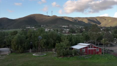 Establishing-aerial-view-rising-above-typical-red-barn-farm-homestead-under-mountain-landscape