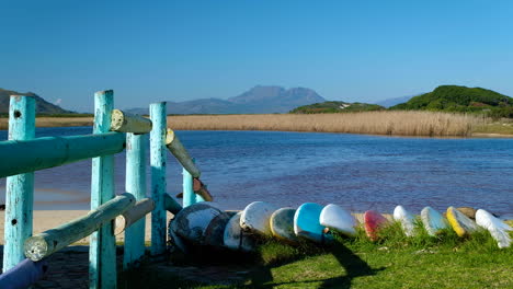 paddle skis stacked on shore next to beautiful lagoon, popular holiday destination, reeds and mountain background