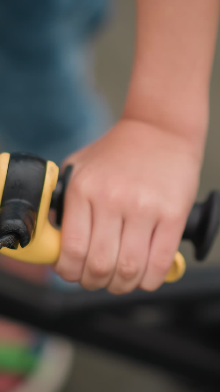 un primer plano de la mano de un niño agarrando el freno de una bicicleta, el enfoque está en la mano del niño y la palanca de freno amarilla, mientras que el fondo permanece borroso
