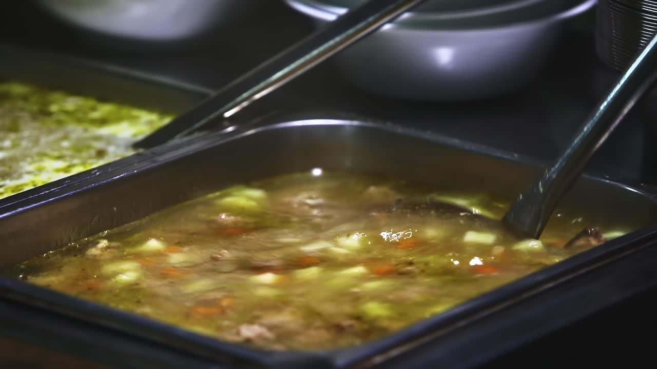Sopa quente em recipiente de metal Concha mexendo caldo com carne e legumes Cozinha de serviço de alimentação, catering, processo de cozimento em close-up Cozinha profissional ou linha de catering Processo de preparação de alimentos quentes